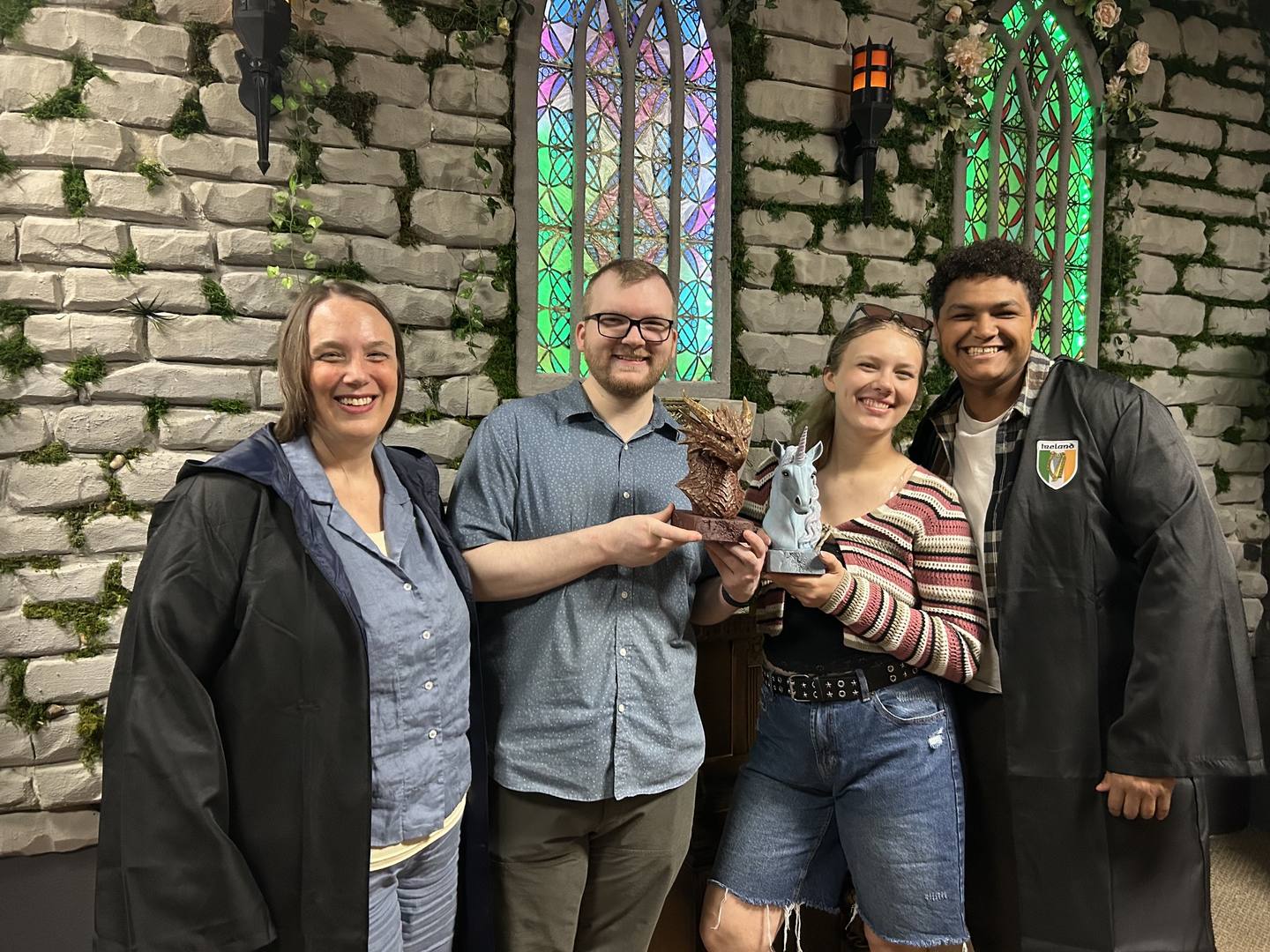 Guests posing with dragon and unicorn statues in front of the stained glass window inside Griffin's Door, the fantasy escape room at Twisted Escape Rooms in Vancouver, WA